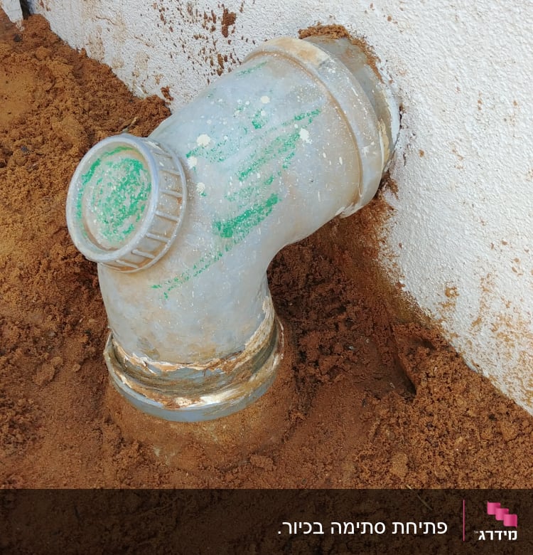 צינור ביוב מתכת מחובר לקיר עם אדמה סביבו